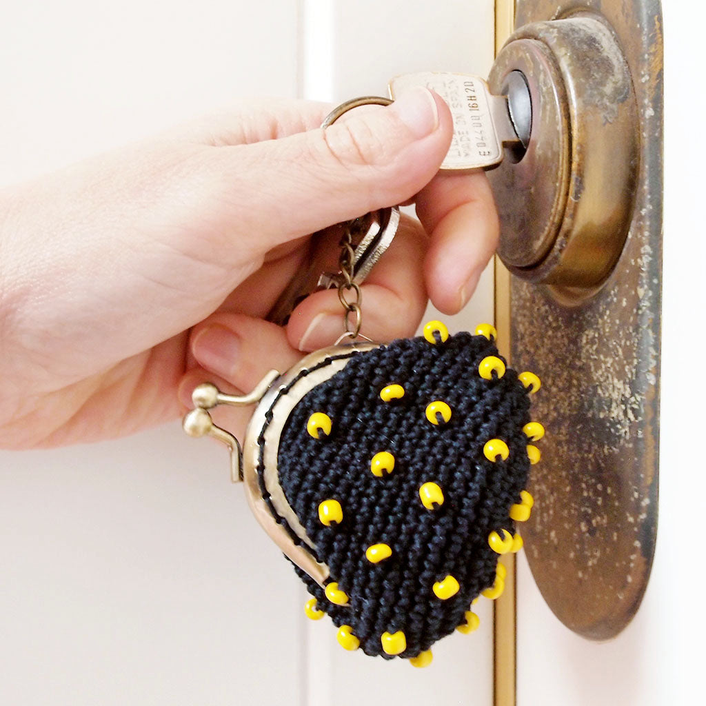 Una mano abre una puerta con una llave con monedero de ganchillo negro con cuentas amarillas