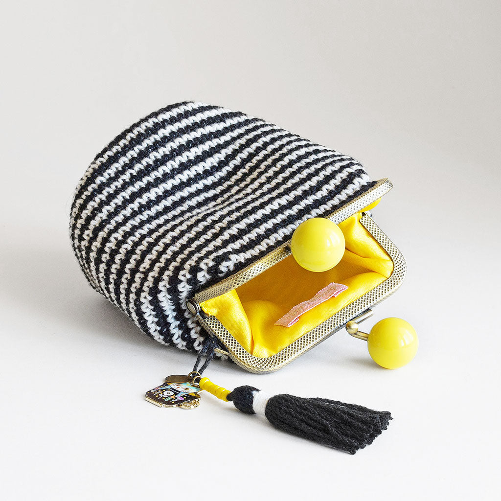 monedero de crochet a rayas blancas y negras con boquilla amarilla tumbado dejando ver su interior forrado de raso amarillo