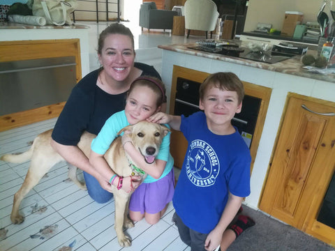 Woman and two young kids pose in a photo with a cream colored dog