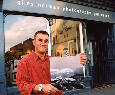 Giles standing outside his gallery holding his first photography book in 2002