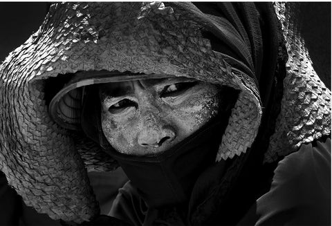 A portrait of a woman wearing a straw hat and a creamy paste on her face with her lips covered.