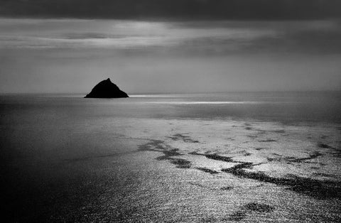 A black and white image of Tearaght Island with sunlight shining down on the surrounding ocean. 