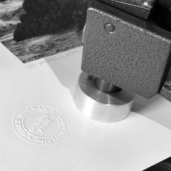 A section of a photographic print with an embossed stamp and an embosser. 