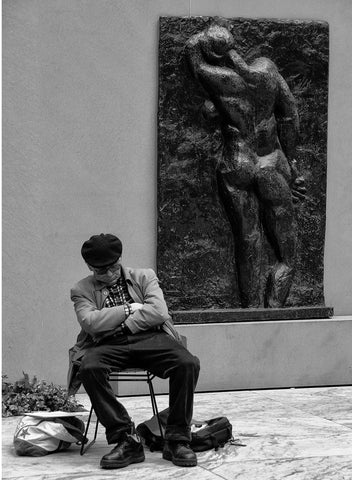 A man taking a nap in MoMA with a sculpture in the background.