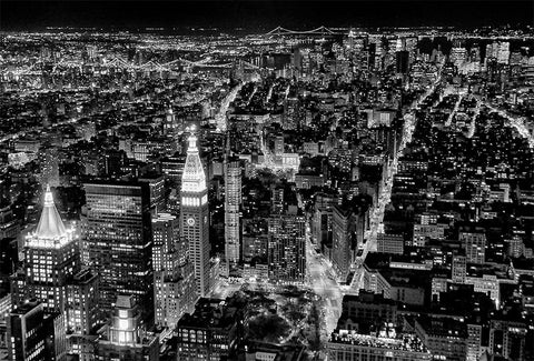 A black and white image of Manhattan at night from an elevated perspective looking down on the skyscrapers. 