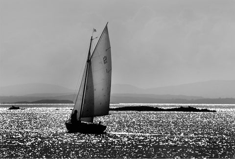 A black and white image of a boat sailing and the sun shining down on the water. 