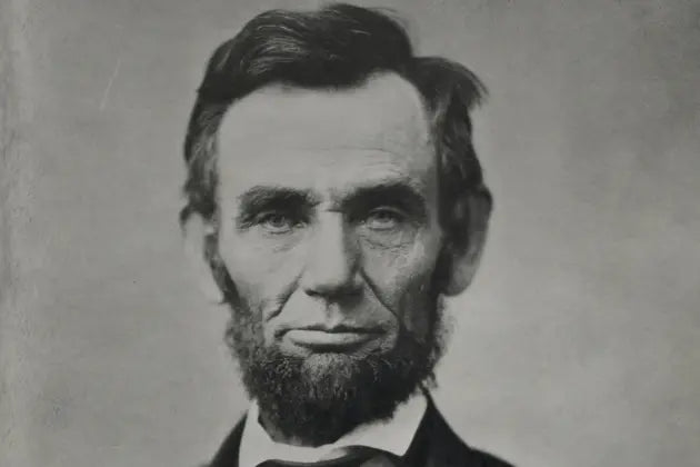 Foto de Abraham Lincoln, em tons de cinza. Lincoln é um homem de meia idade que usa barba Old Dutch e olha direto para a câmera.