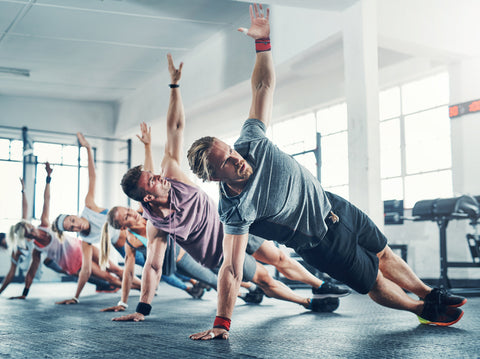 A group of people perform side plank at a gym class