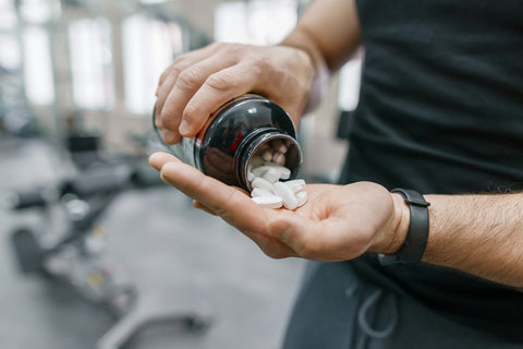 a man pours supplements into his hand from bottle in the gym