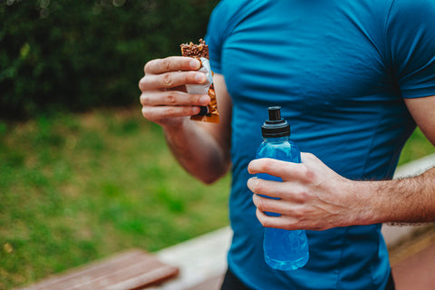 A close up of a runner's chest, he's holding a protein bar and a water