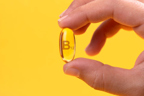 Vitamin B-12 capsule being held up against a yellow background