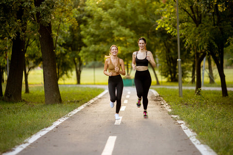 Two woman running down a road through some trees