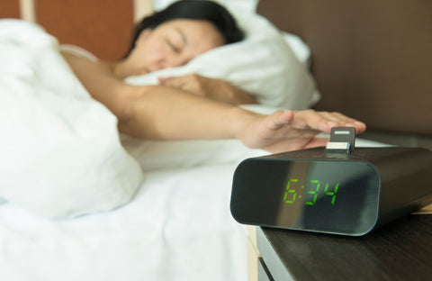 woman in bed hitting the snooze button on her alarm clock