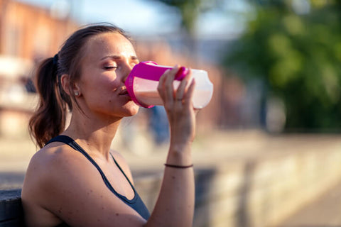 Woman with brown pony tails is outside drinking a protein shake