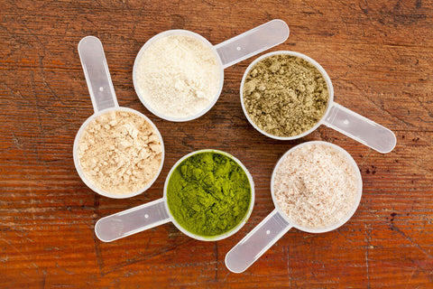 scoops of whey and vegan protein side by side on a wooden table