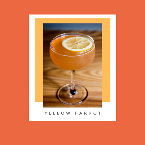 Orange cocktail in a coupe with a lemon wheel floating on top on a wood grain counter. 