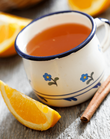 A hot toddy mug with slices of orange and cinammon surrounding it.