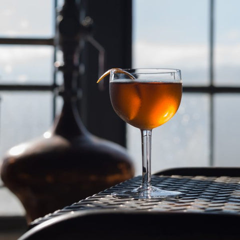 Beautiful orange cocktail against the backdrop of windows, out of which you see light blue sky and clouds.