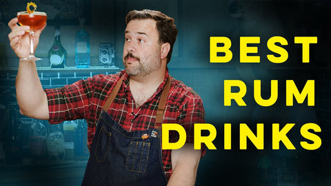 Image of a man in a work apron and a checkered shirt holding a cocktail and gazing at it against a blue green backdrop with large bright yellow text: BEST RUM DRINKS