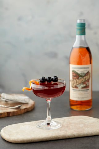 Cocktail garnished with three cherries on a wood cutting board. Yellowstone Single Malt in the background.