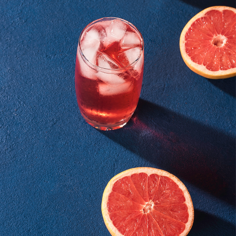 deep blue backdrop with bright slices of grapefruit and a deep pink drink with ice in it, shot from above