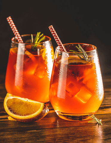 two glasses of deep ruby red spritzes with a red and white straw and a blood orange garnish