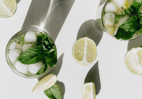 flat lay view of two mojitos with cut lime pieces and mint leaves scattered about.