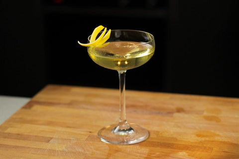 Simple elegant cocktail with clear spirits in a coupe and a lemon twist on a cutting board.