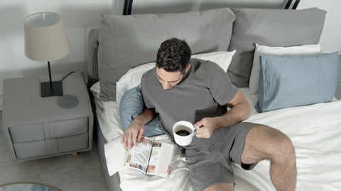 Male model lying on bed having coffee wearing restlab's Equilibrium Sleep Set
