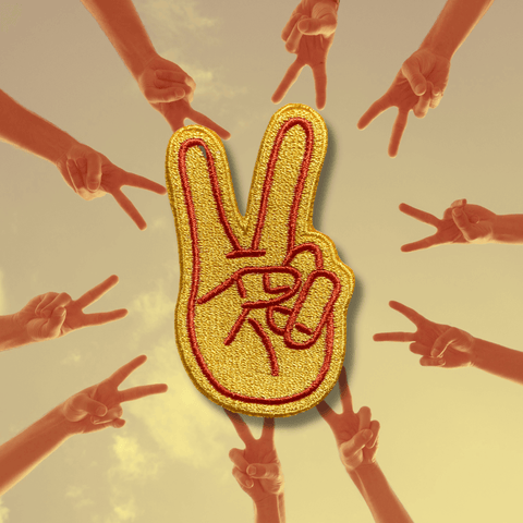 an image of a yellow patch with red outline shaped like two fingers giving the peace sign. The patch background is a photo of 10 arms in a circle at dusk shot from below all giving the peace sign.