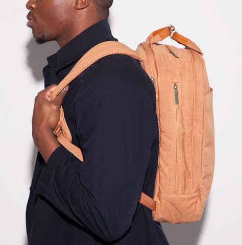 a black man facing left carries a Day Owl laptop backpack on his back. He wears a dark sweater.