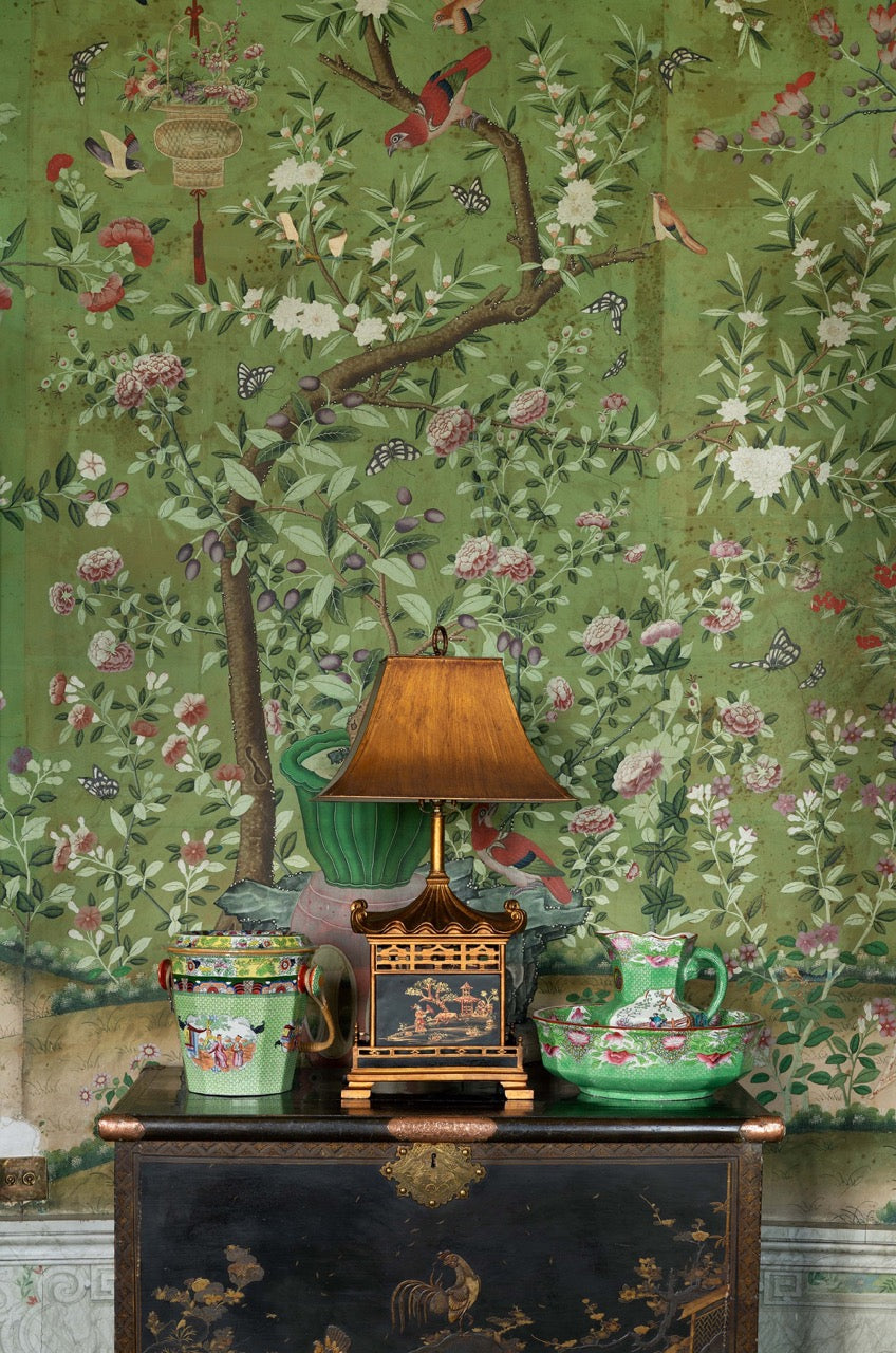 Green chinoiserie wallpaper behind an antique table, lamp, and ornaments at Belvoir Castle