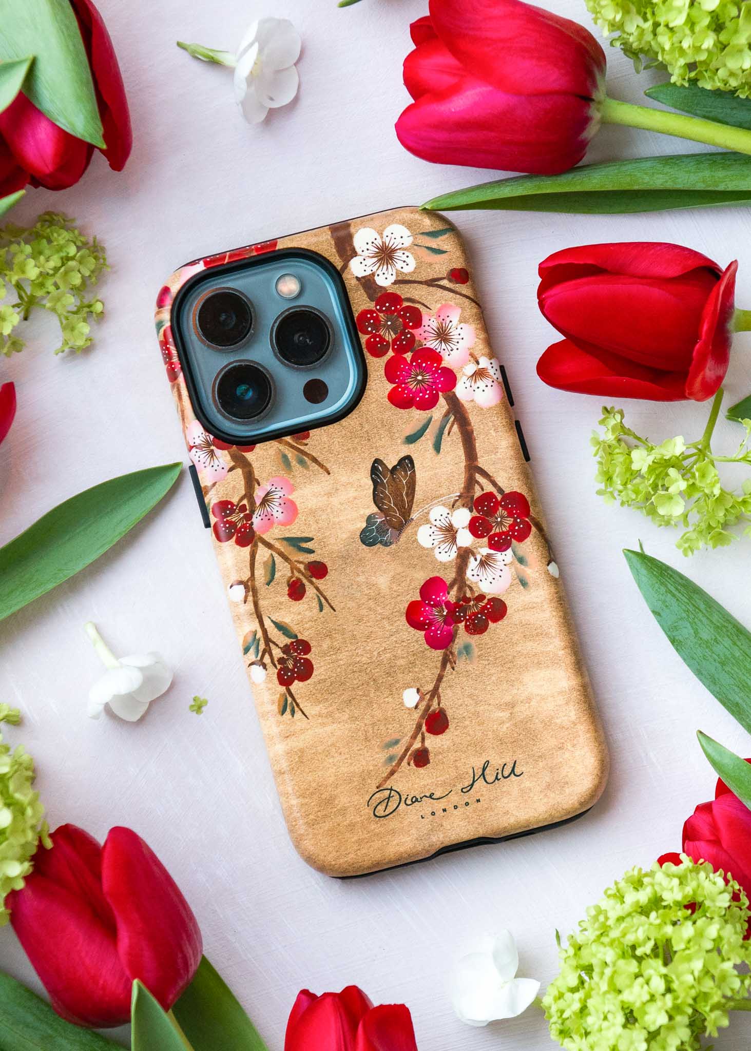 Luxury chinoiserie phone case design by Diane Hill on a flat background surrounded by red flowers