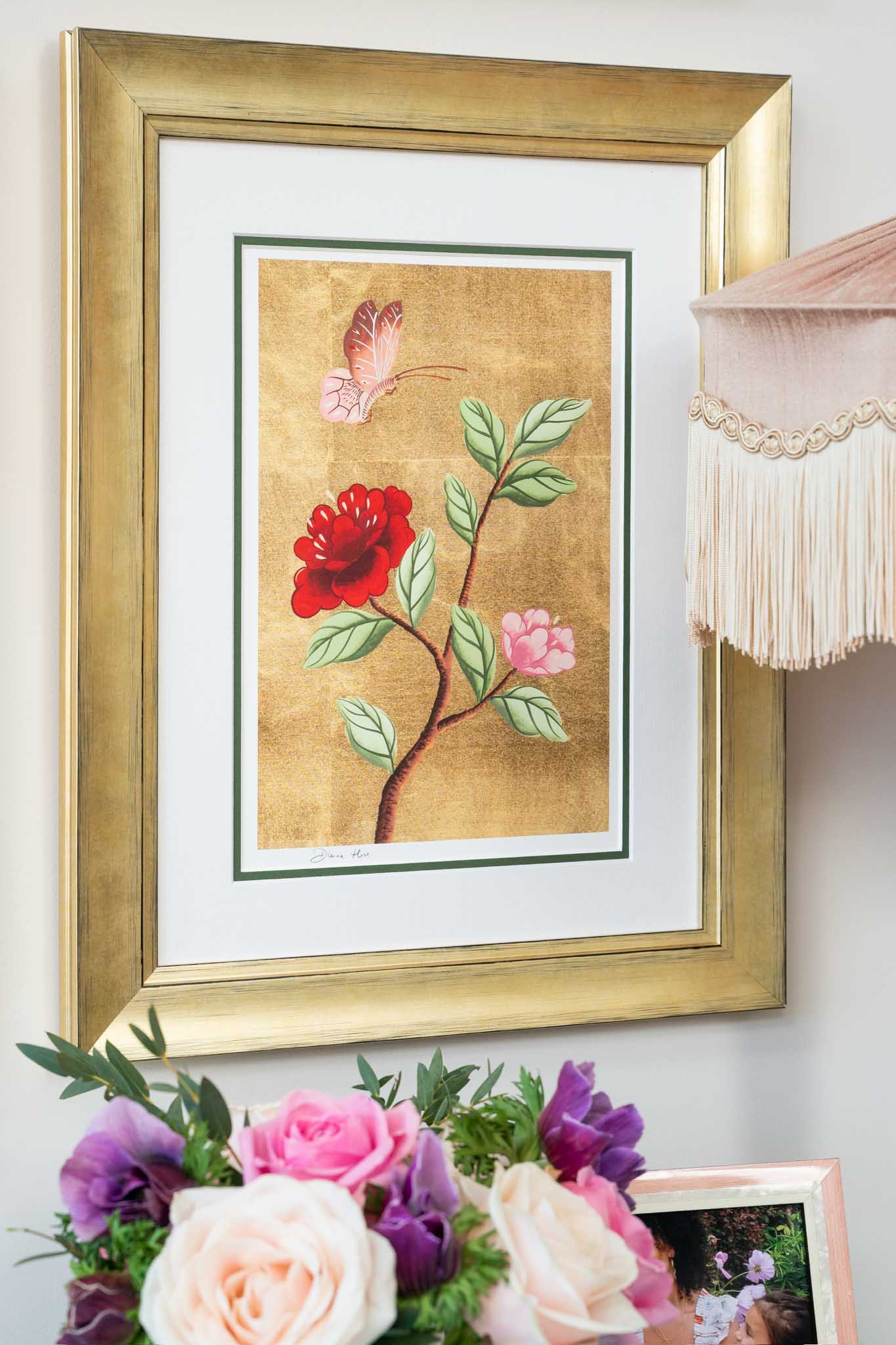Diane Hill's 'Chloe B' chinoiserie art print on a wall in a gold frame with a tassel lamp and flowers just in frame