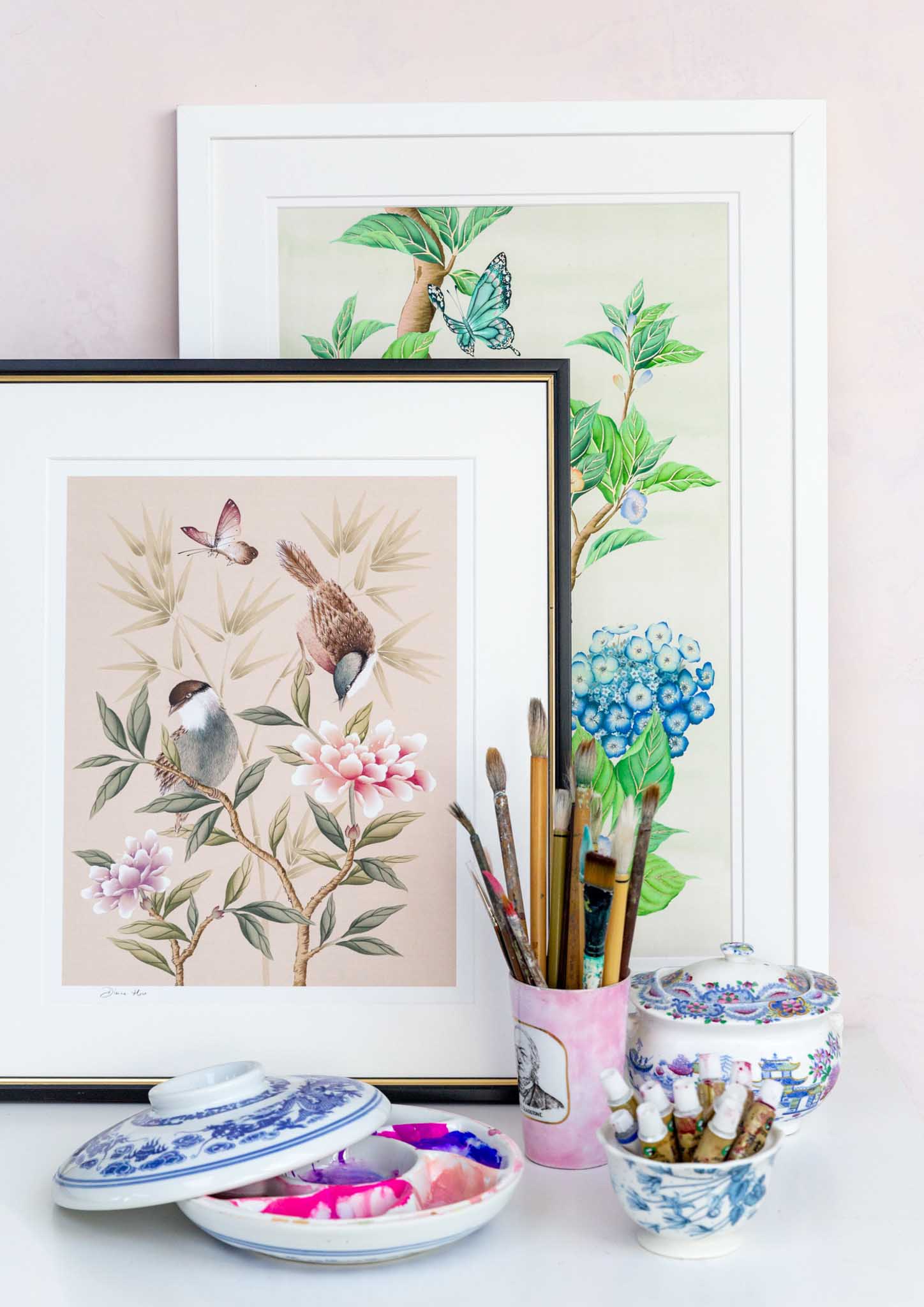 Diane Hill chinoiserie art prints in frames on a desk with paintbrushes and a palette containing paint