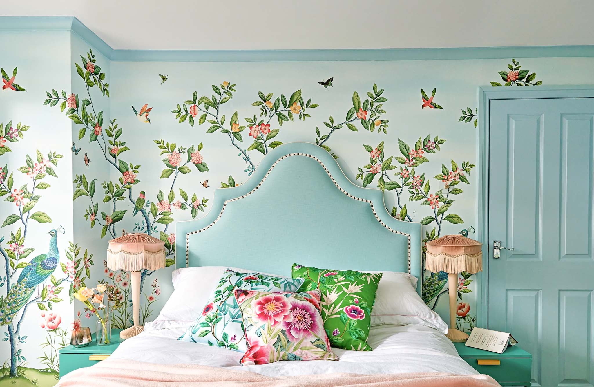 Chinoiserie bedroom blue floral wallpaper with large upholstered headboard and colourful chinoiserie cushions to match