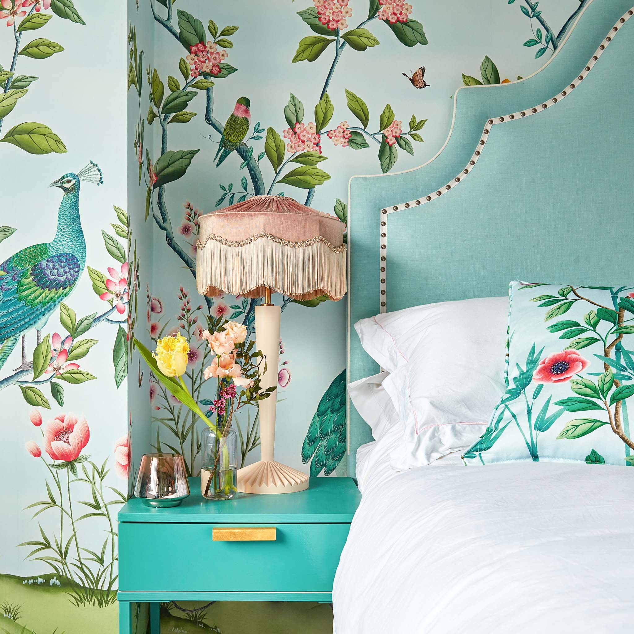 Chinoiserie bedroom bright colourful wallpaper with blue headboard and bedside table with pink lamp