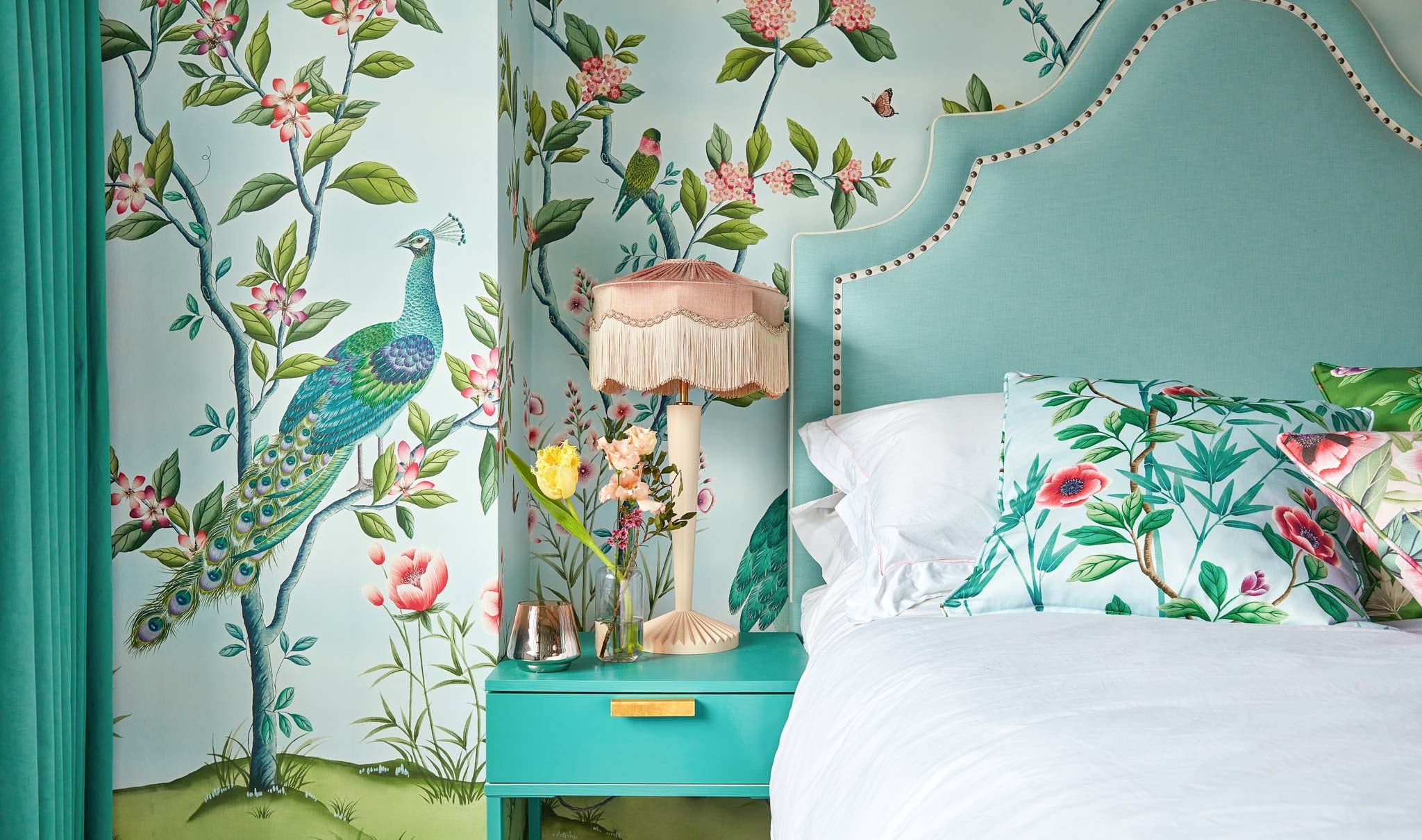 Florence blue Chinoiserie wallpaper peacock flowers and trees in bedroom setting with chinoiserie cushions blue headboard and pink beavamp lamp