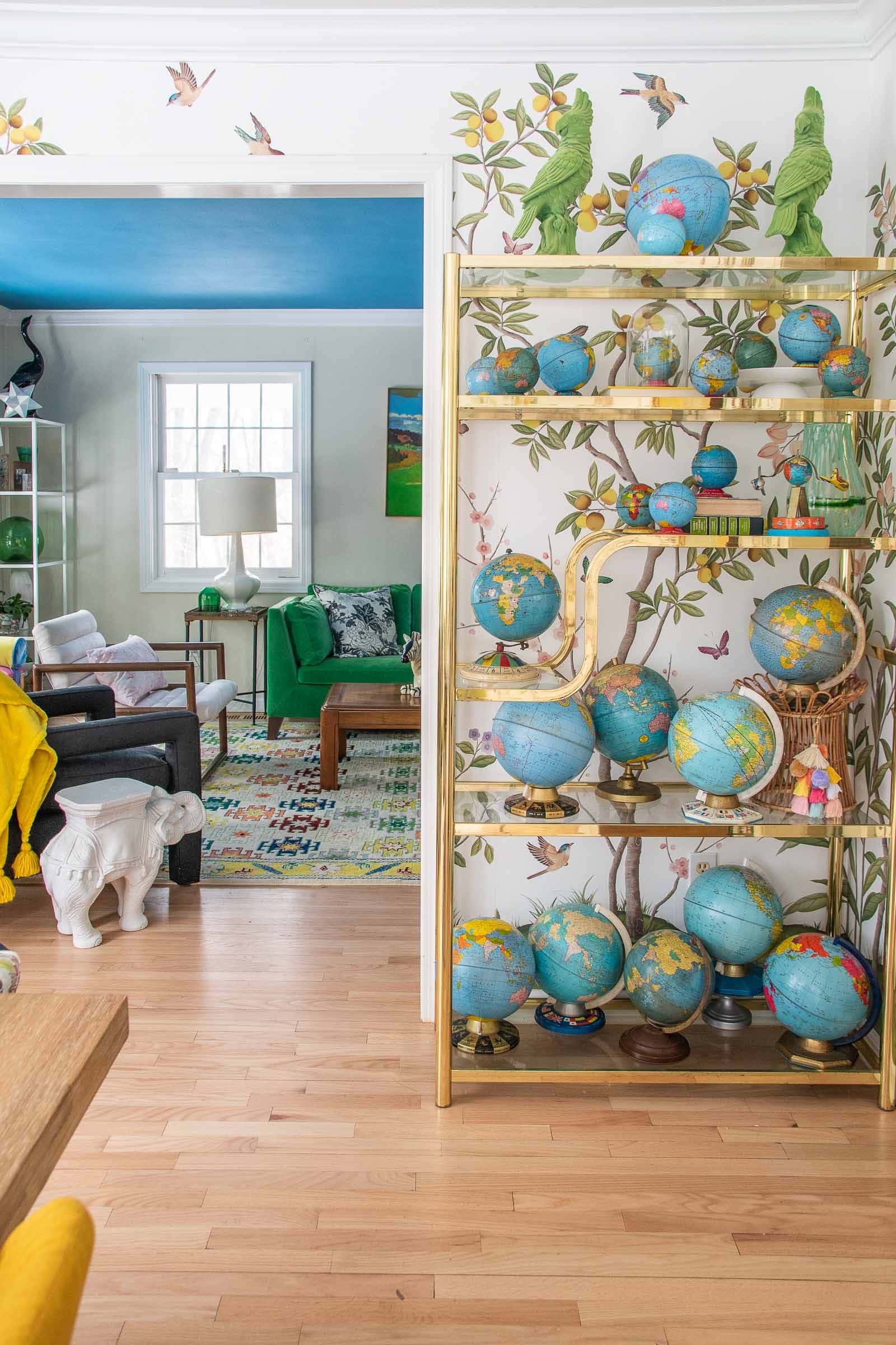 Maximalist style home with ornamental globes of various sizes in front of Diane Hill's chinoiserie wallpaper design for Rebel Walls