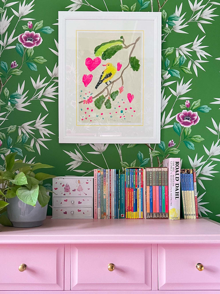 Pink painted chest of drawers and green chinoiserie wallpaper with childs artwork framed