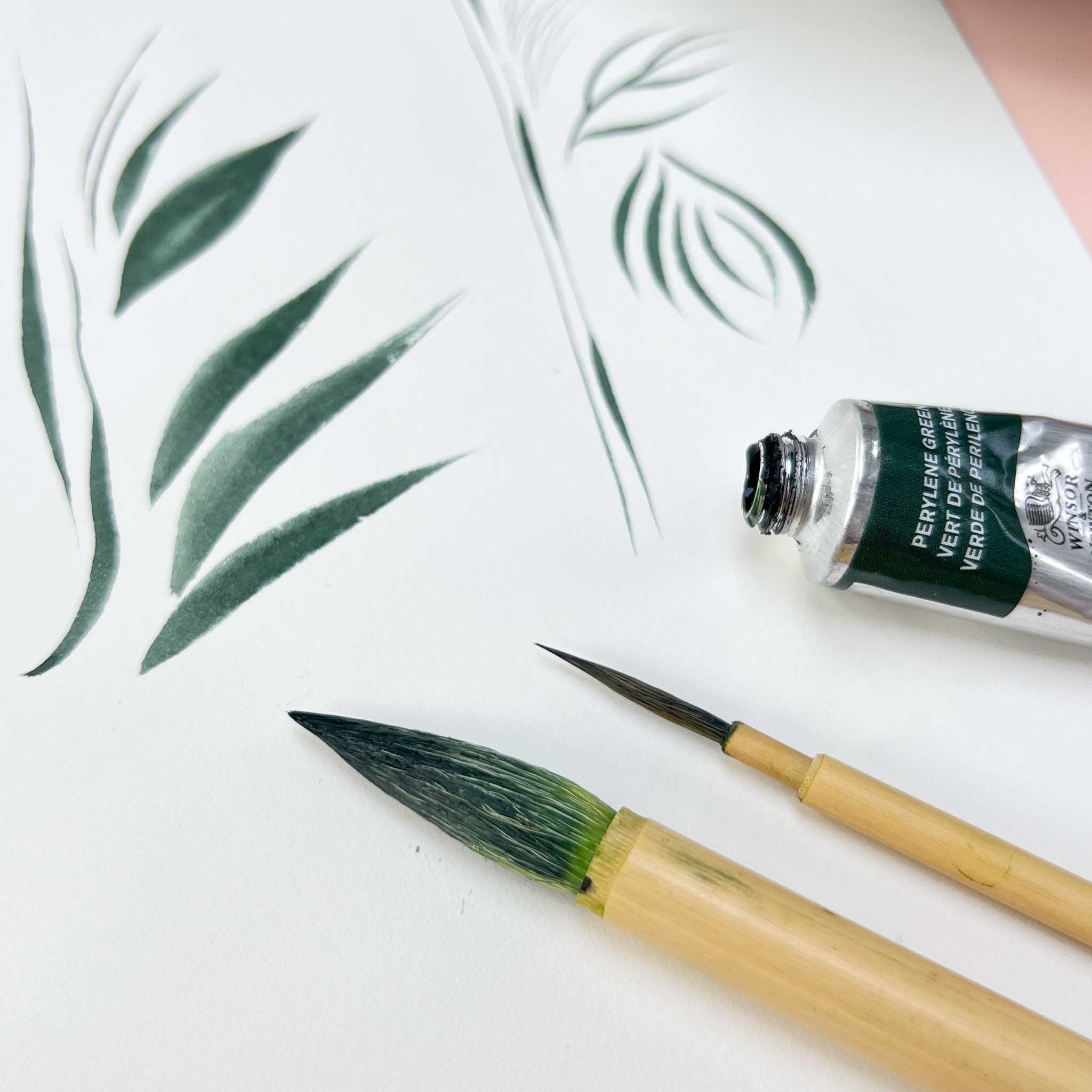 two chinoiserie paintbrushes on paper next to a tube of paint