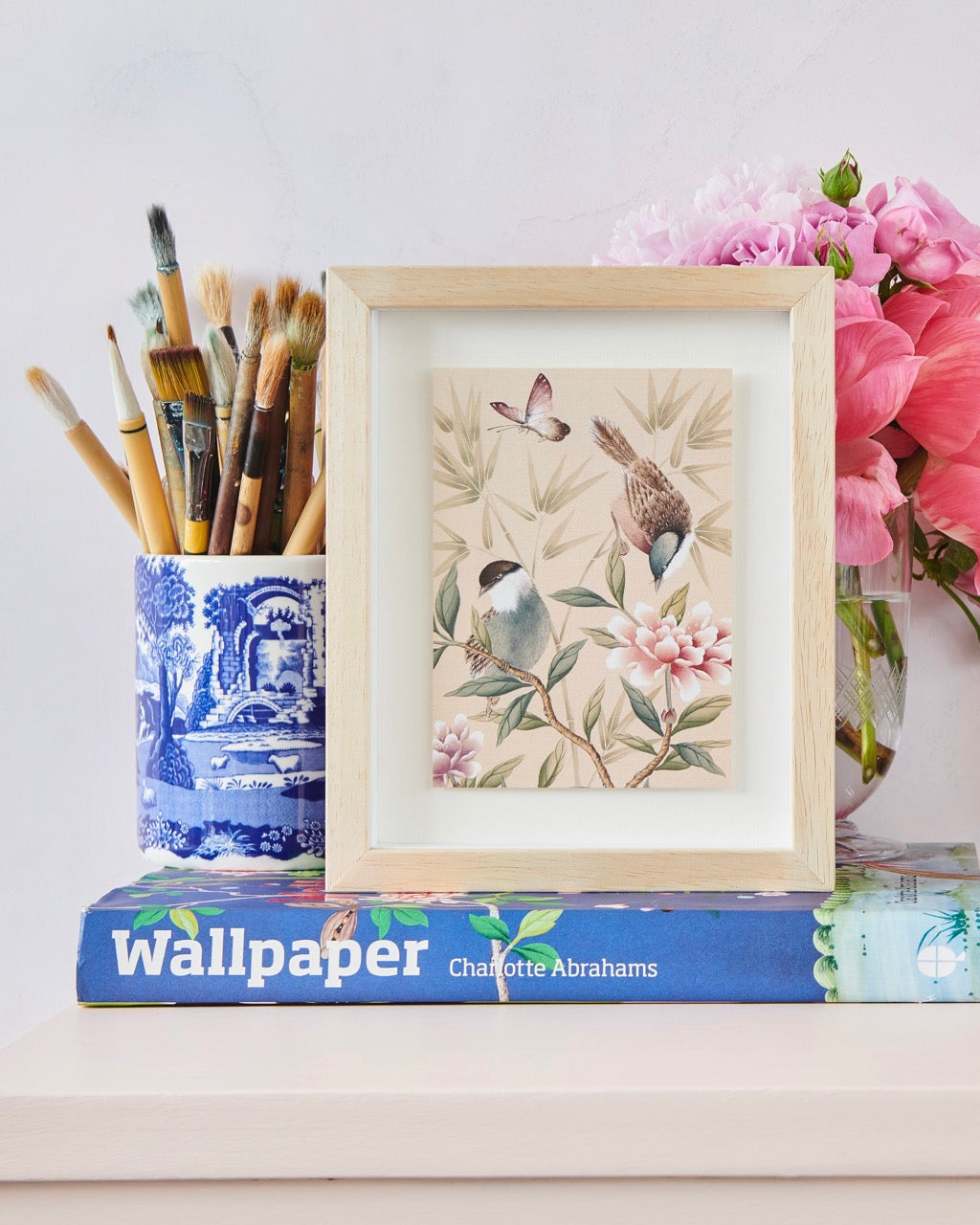 Diane Hill's mini chinoiserie art print in a frame on a desk on top of a book with a pot full of pencils next to it