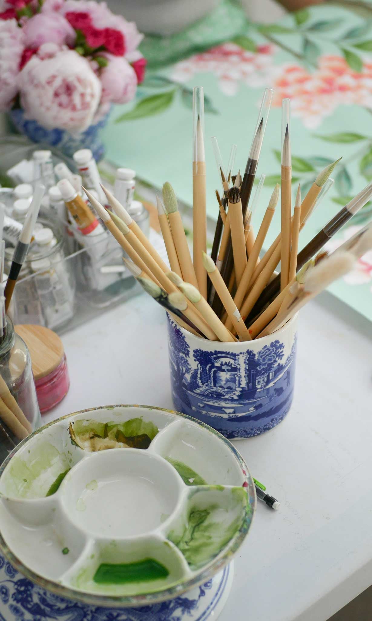 Paintbrushes in a pot next to a paint palette containing green paint