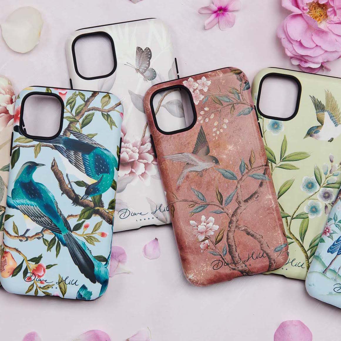 four chinoiserie style phone cases designed by Diane Hill on a flat surface with flowers