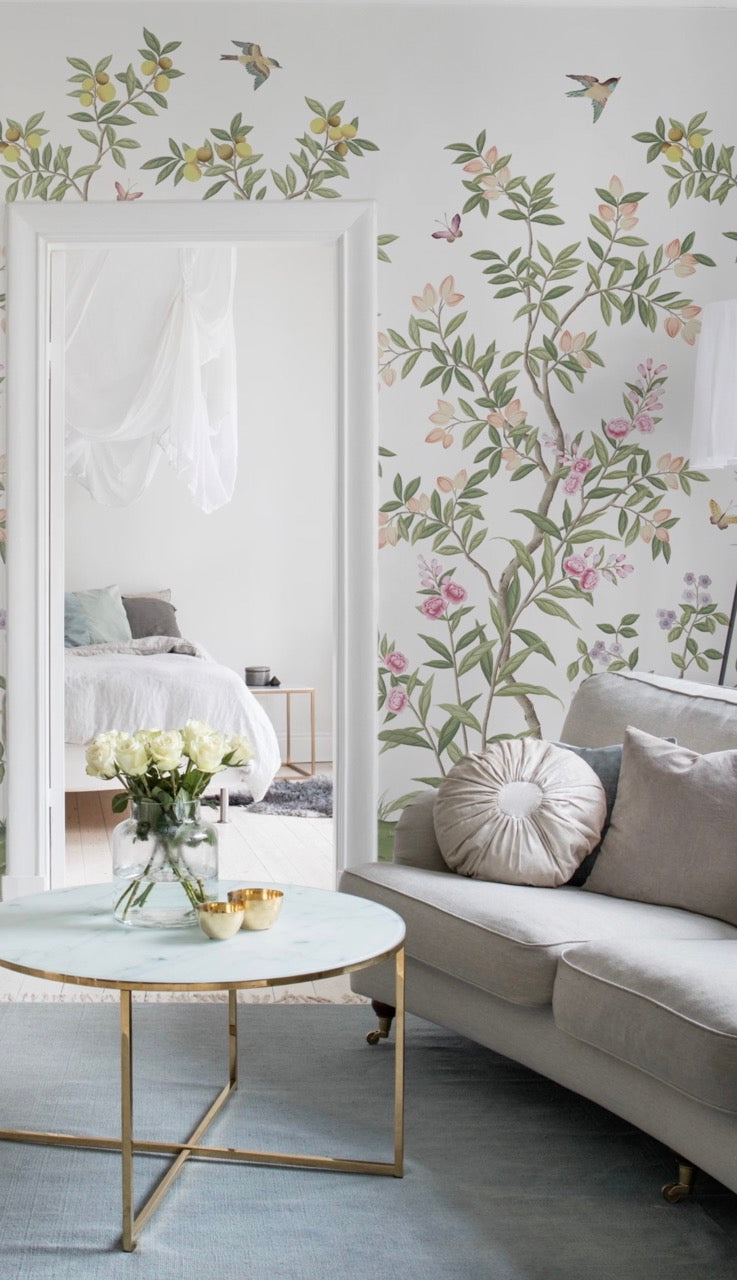 Diane Hill's 'Chinoiserie Chic' wallpaper for Rebel Walls in a bedroom with a mirror, sofa, and round table with flowers on top