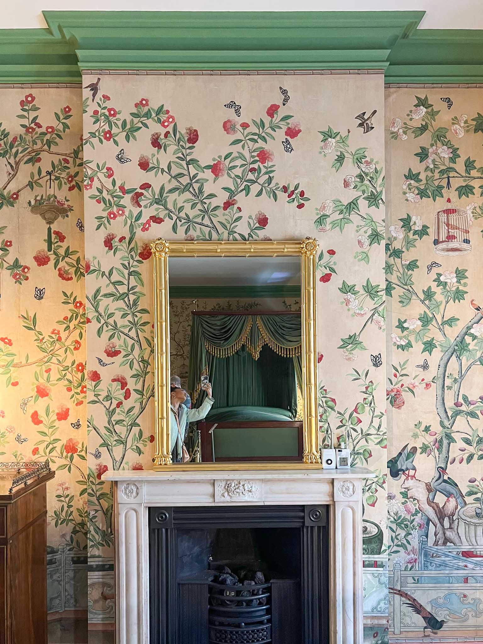 Chinoiserie wallpaper inside Queen Victoria's bedroom in Brighton Pavilion in front of a gold mirror sat on the fireplace