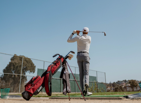 guy playing golf at the range with his red Loma bag