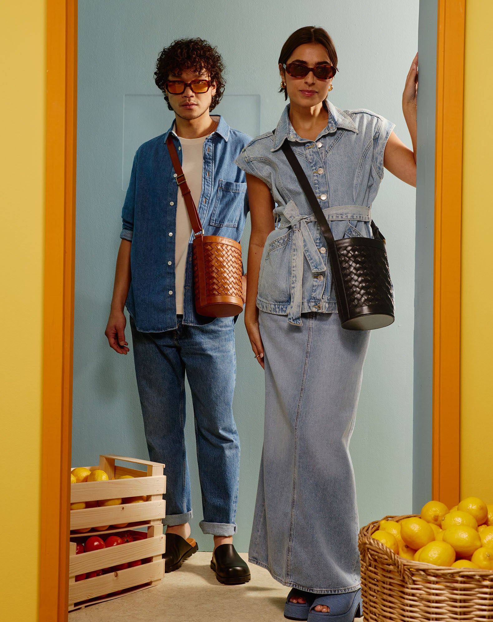 Campaign image featuring fresh fruit and citrus colours, a male and a female model wearing black and brown woven bucket bags