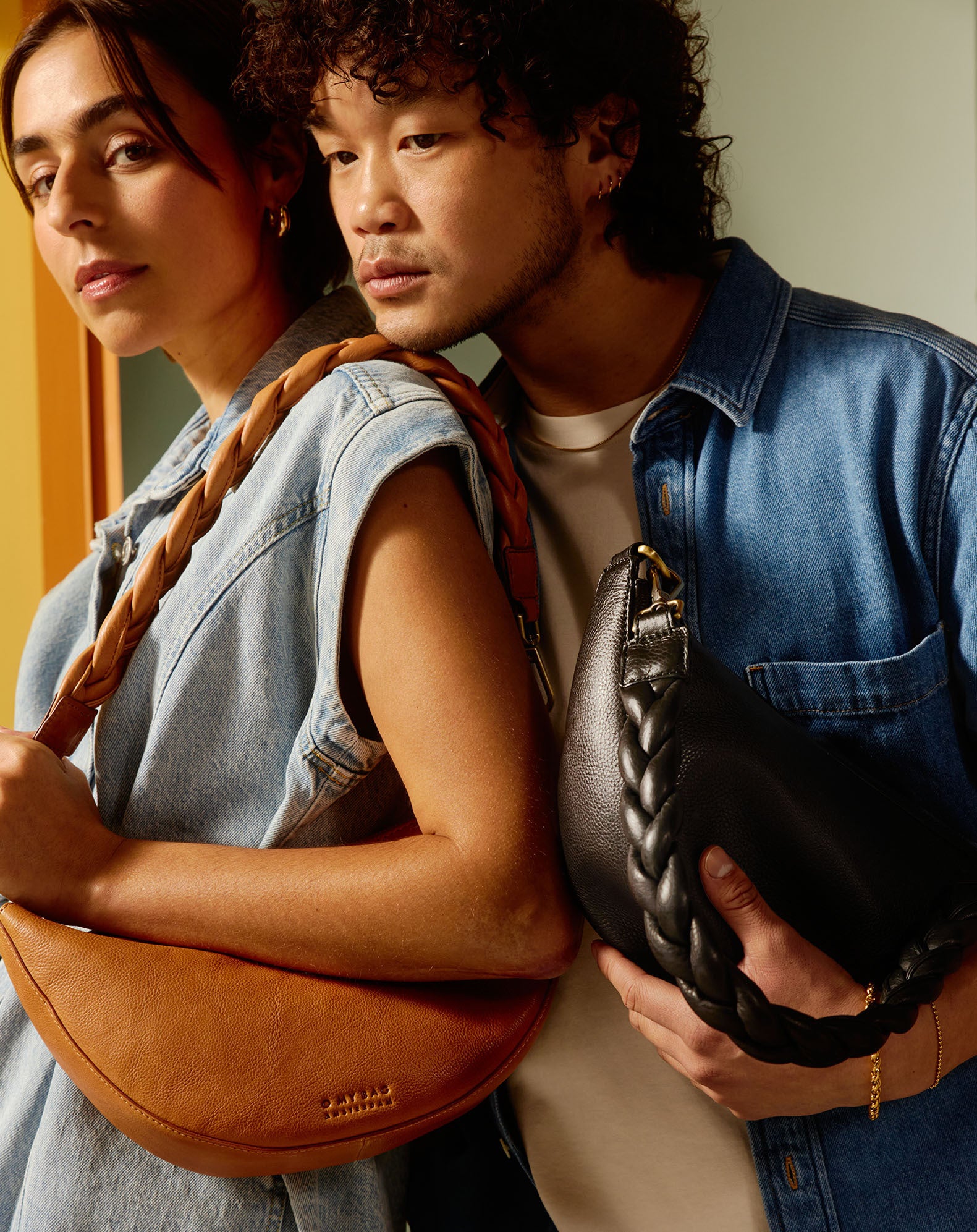 Campaign image featuring fresh fruit and citrus colours, a male and a female model wearing black and brown soft grain bum bags with braided straps