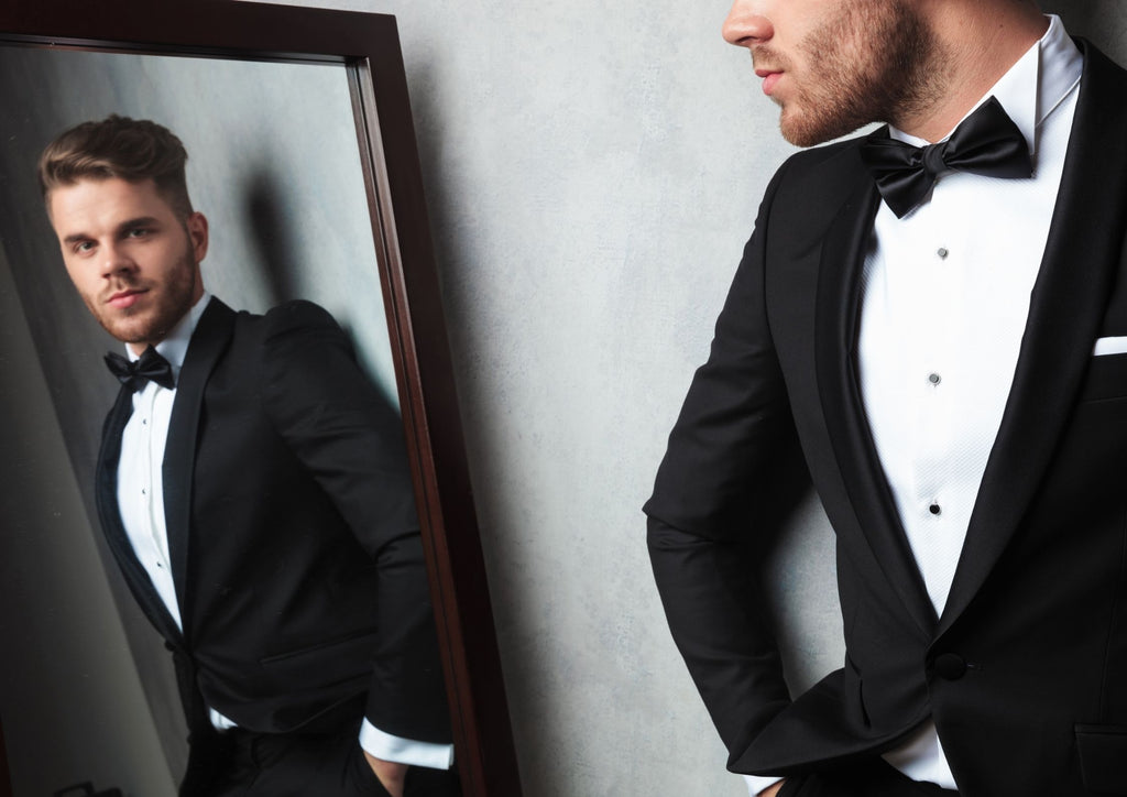man in tuxedo looking at mirror